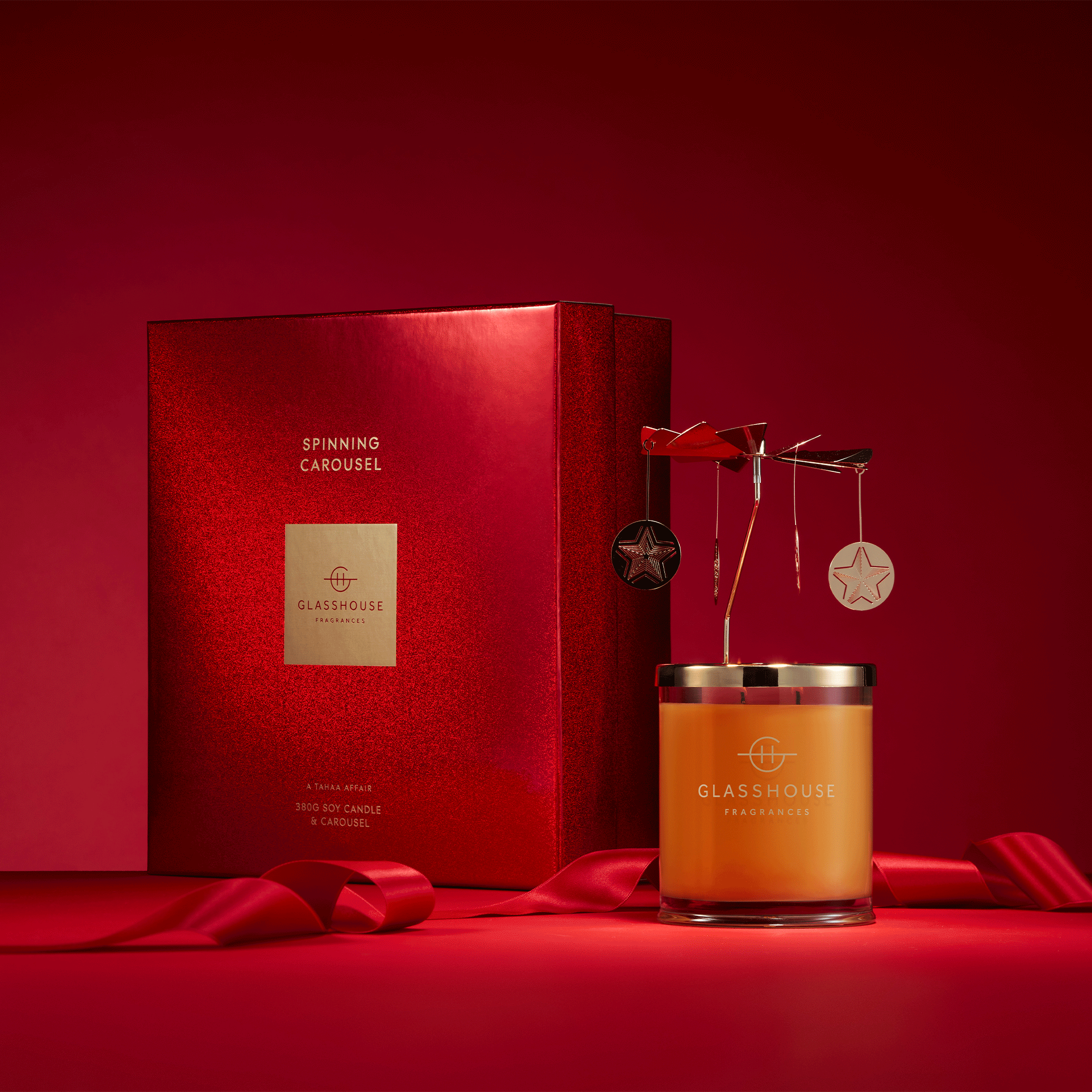 Glasshouse Fragrances A Tahaa Affair Vanilla Caramel 13.4oz Soy Candle and animated Spinning Carousel with box on red backdrop